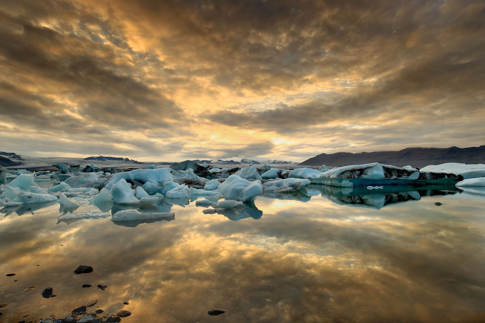 Die Lagune des Jökulsárlón Gletschersees voller Eisberge bei Sonnenuntergang mit dramatischen Wolken, die sich im See spiegeln.