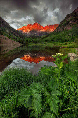 Die Maroon Bells bei Aspen in Colorado spiegeln sich bei Sonnenaufgang tiefrot im Maroon Lake.