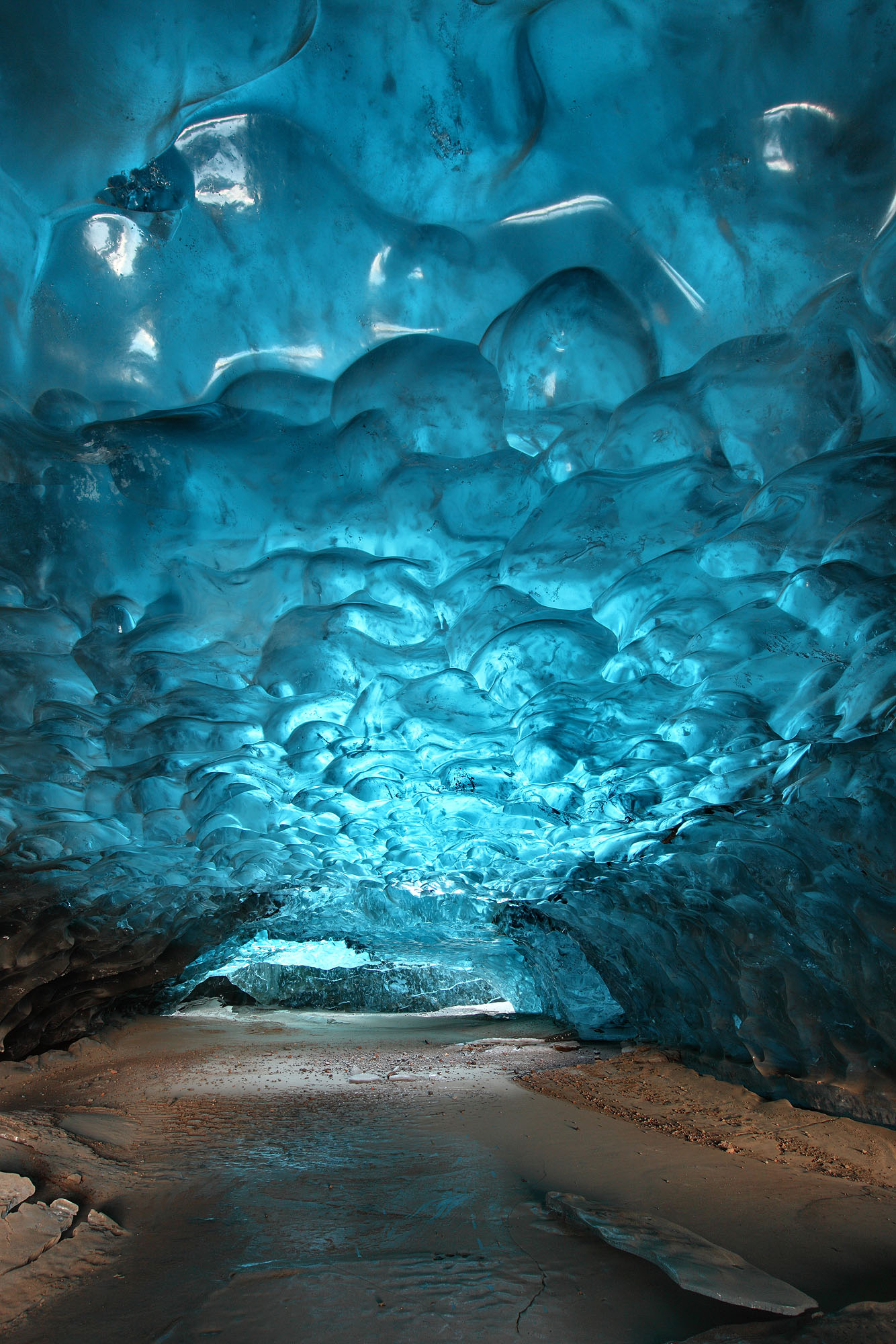 Otherworldly appearing and awe-inspiring ice cave tunnel within Svínafellsjökull glacier in Skaftafell, Iceland, with deep-blue meltwater shapes