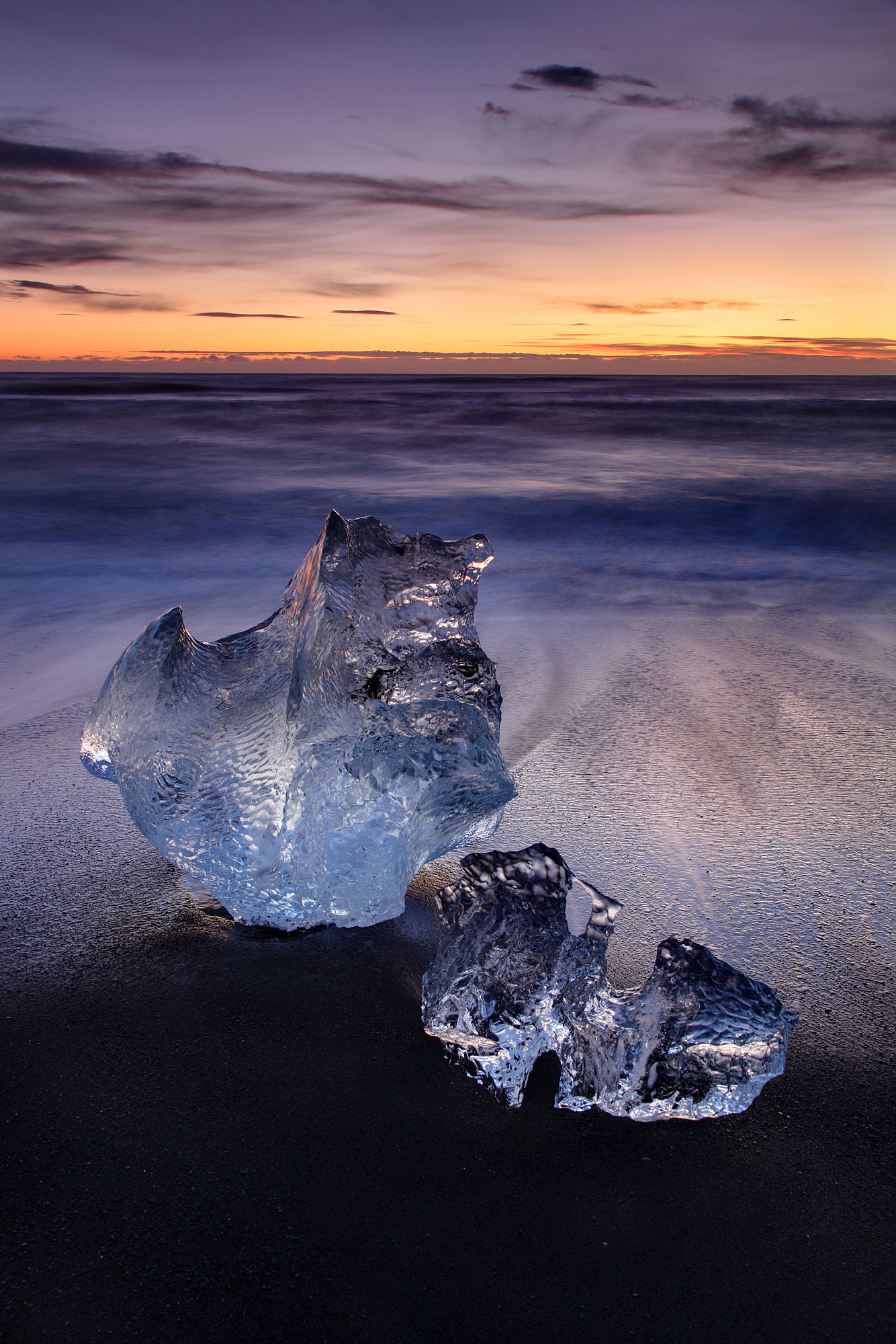 Two small icebergs are beached at low tide on the Jökulsárlón Strandur coastline in wintertime Iceland.