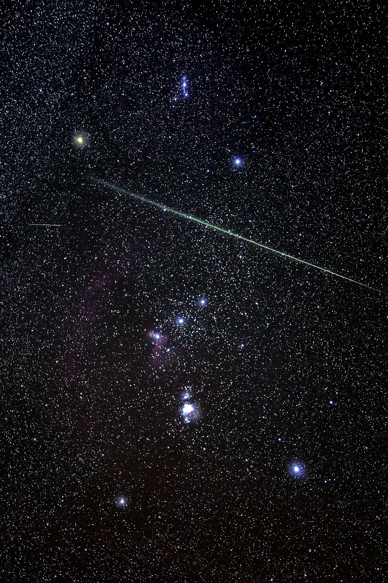 A bright Leonid shooting star falls through the Orion constellation with a bright green head and orange glowing trail