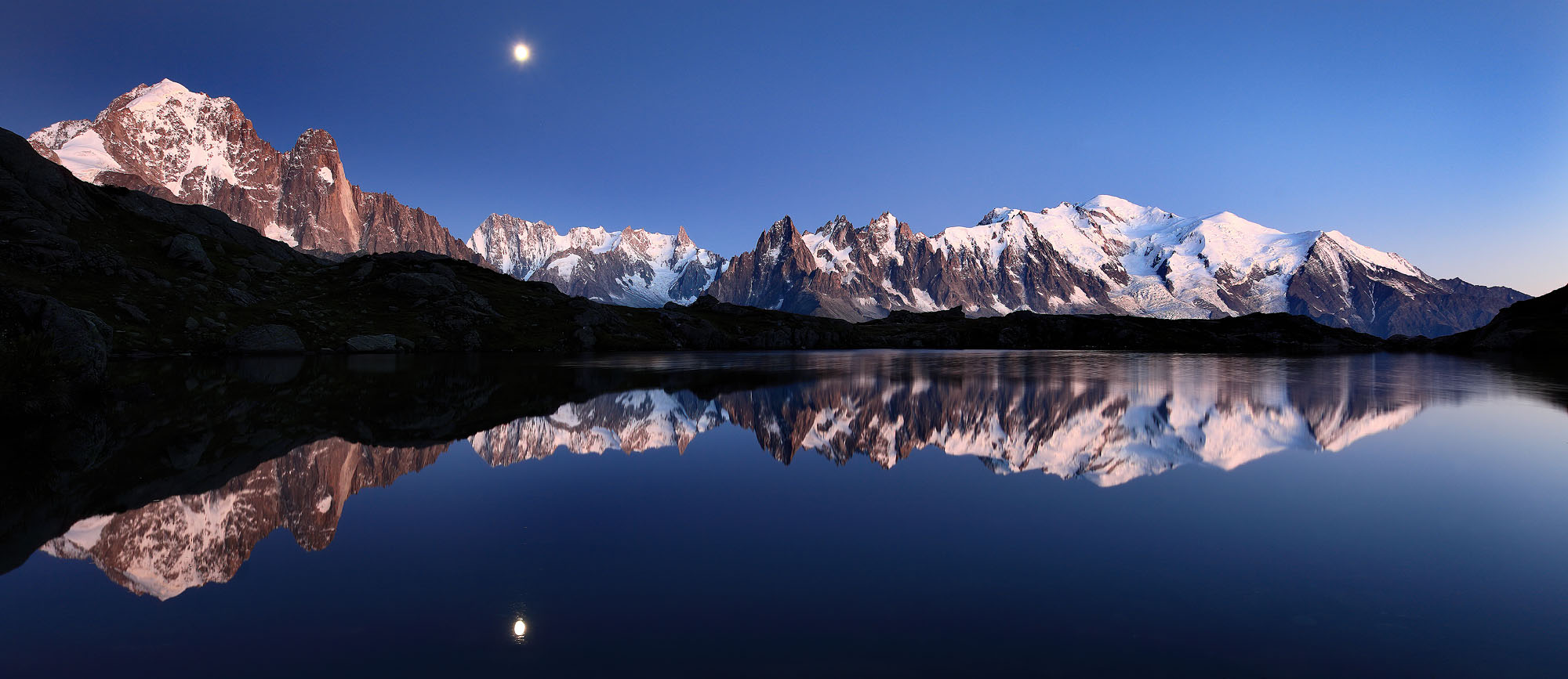 At dusk Lac de Cheserys in the French Alps is reflecting the Mont Blanc massif with the rising moon